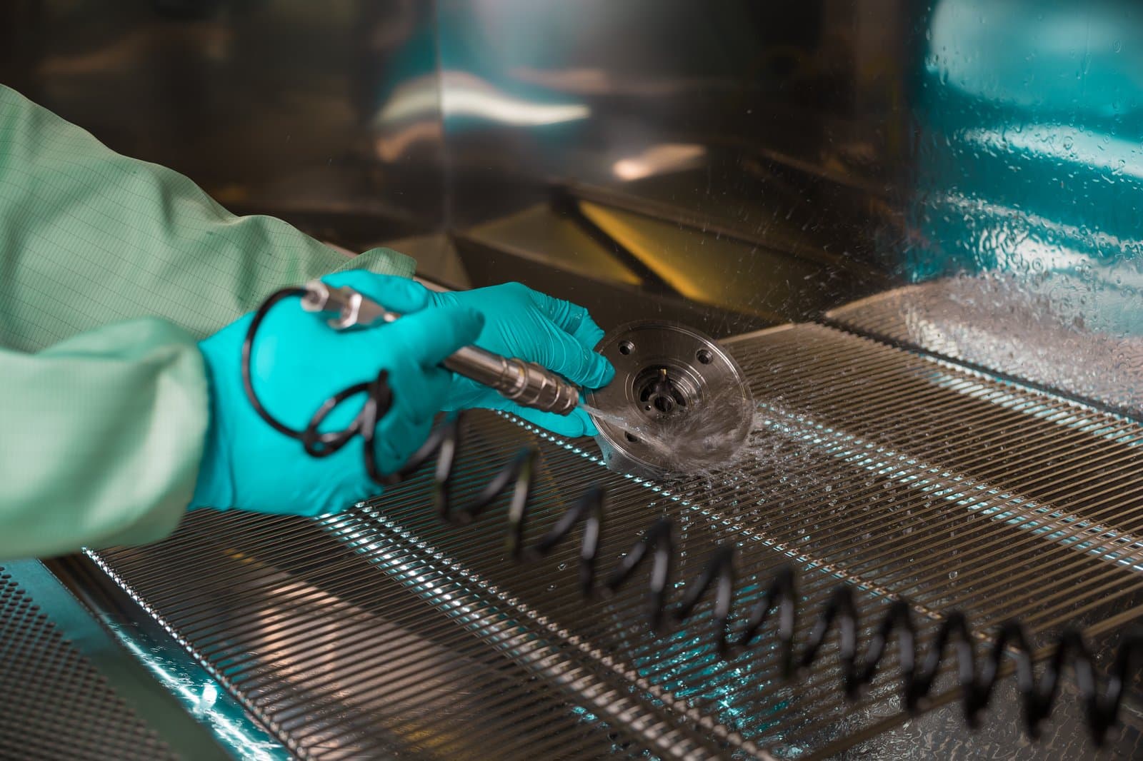 Klarwin technical cleanliness lab — gloved hands rinsing a component over the extraction grate per ISO 16232