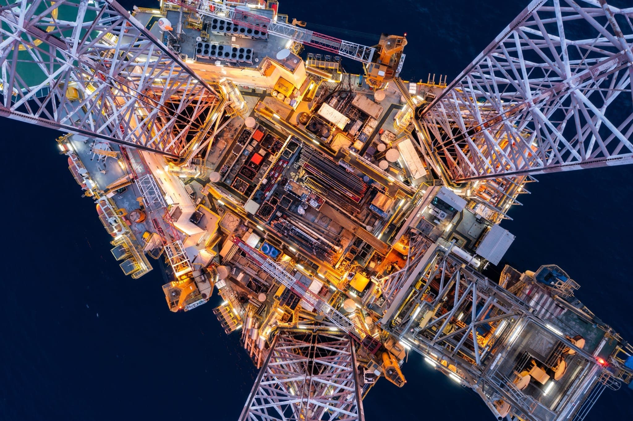 Aerial top-down view of an illuminated offshore oil rig at night