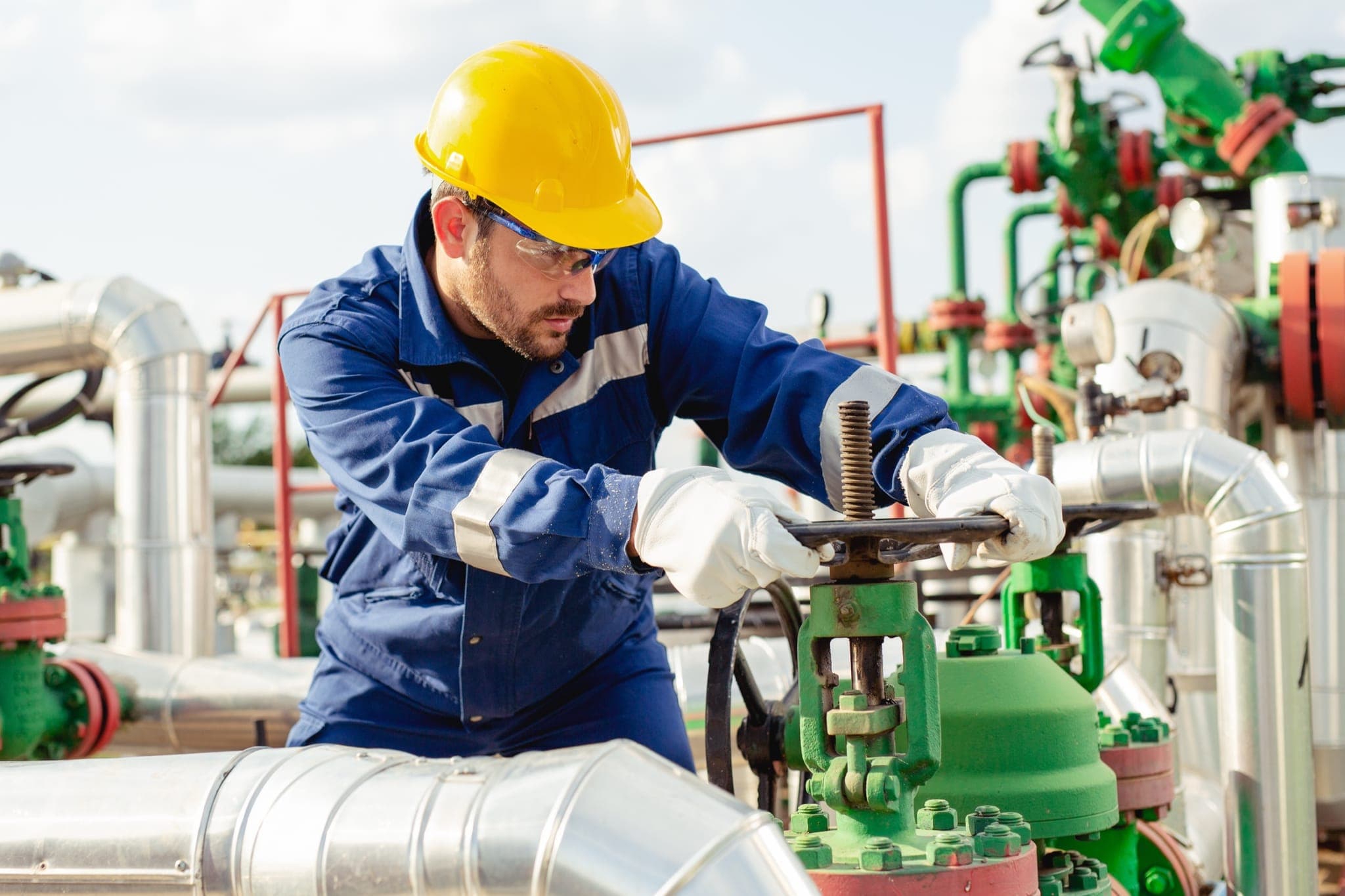 Oil and gas technician operating a valve on a refinery pipeline