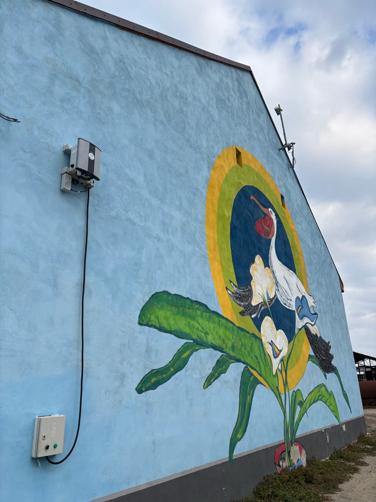 O stație Oizom Polludrone montată lângă o pictură murală de mediu cu un stârc, pe o clădire din județul Timiș