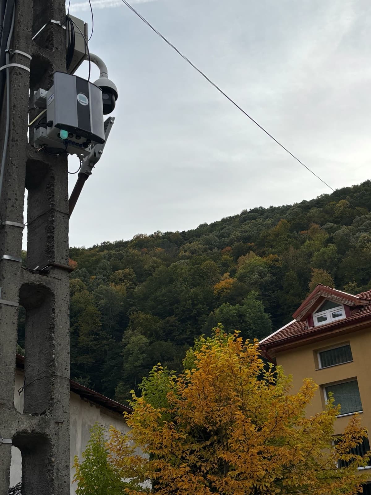 O stație Oizom Polludrone montată sus pe un stâlp de beton, cu un deal împădurit în spate, în județul Timiș